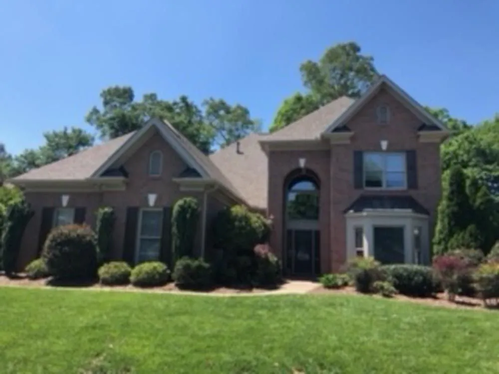 Brick house with green lawn and bushes under a blue sky.