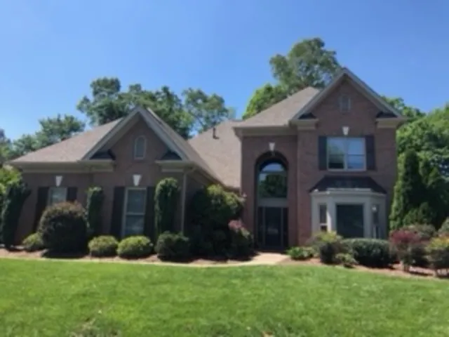 Brick house with green lawn and bushes under a blue sky.