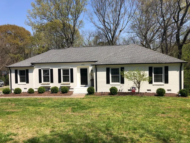 White brick ranch-style house with black shutters, gray roof, and green lawn.